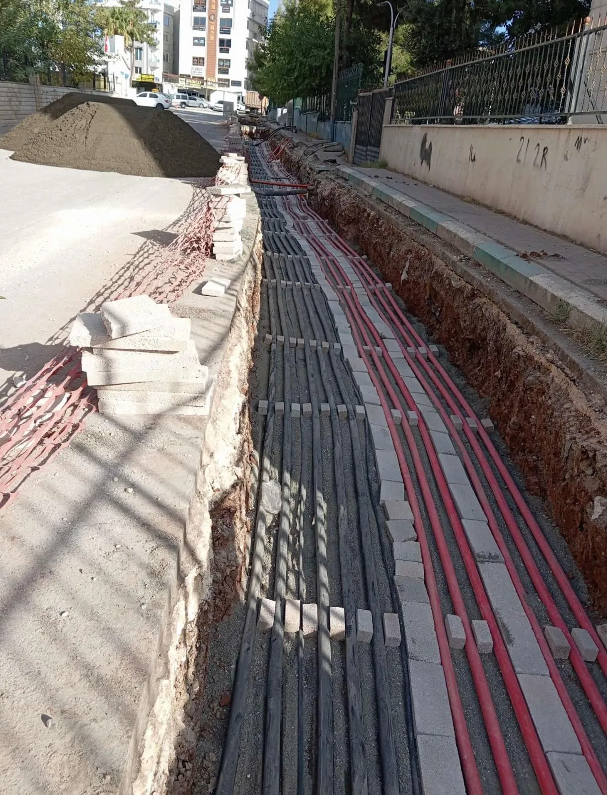 Sokakta açılmış derin kanalda kırmızı koruge borular ve kablolar